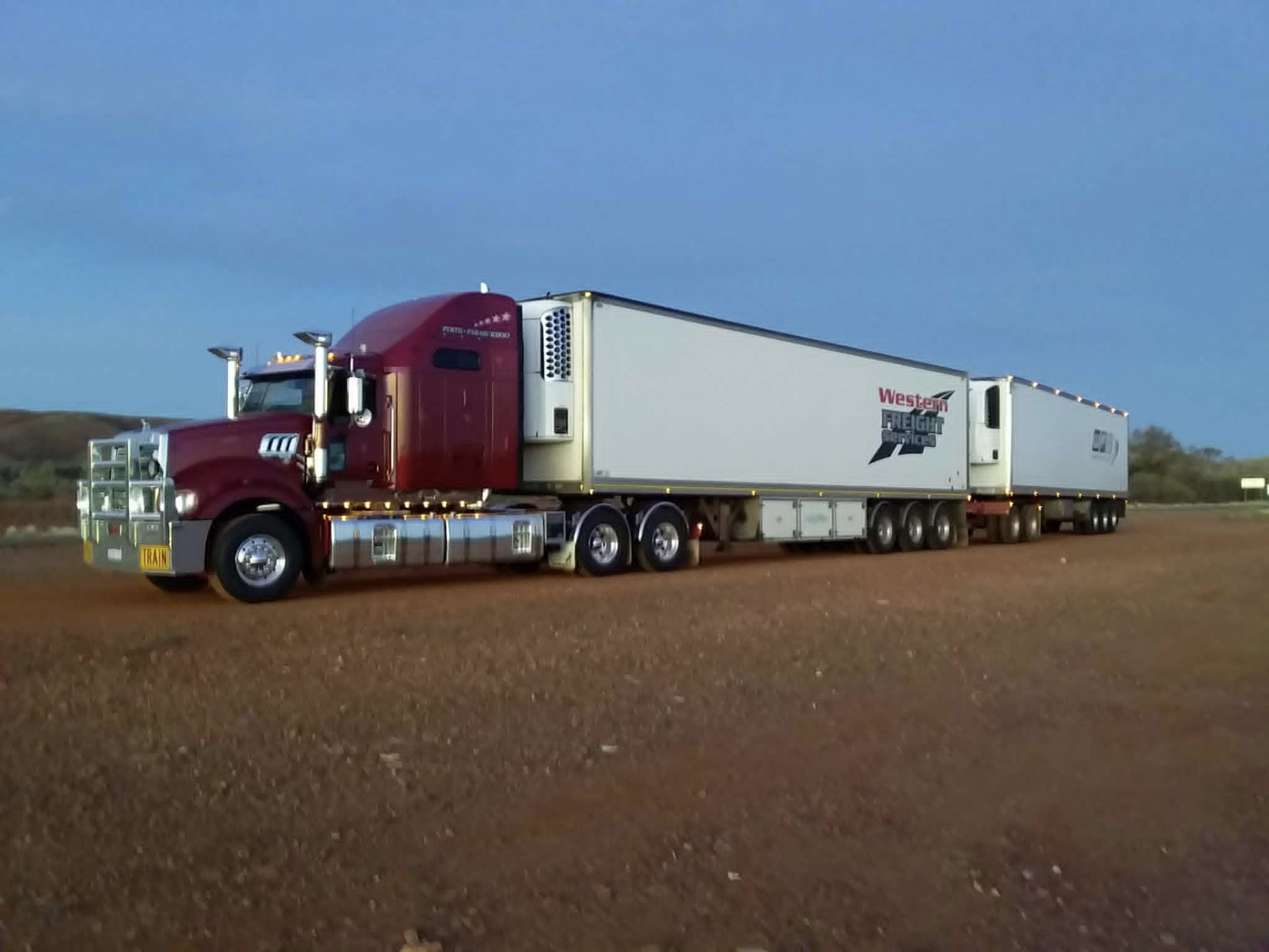 WFS road train with two refrigerated trailers parked on red outback dirt at dusk
